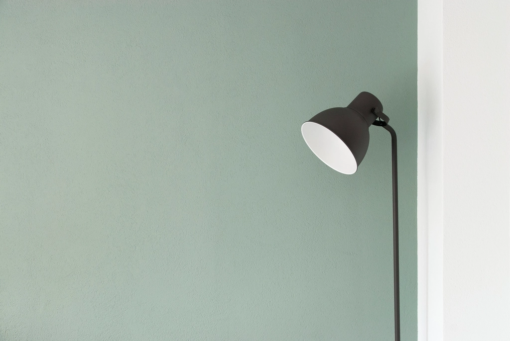 Lampadaire allumé dans l’angle d’une pièce, abat-jour clair et lumière dirigée vers le mur