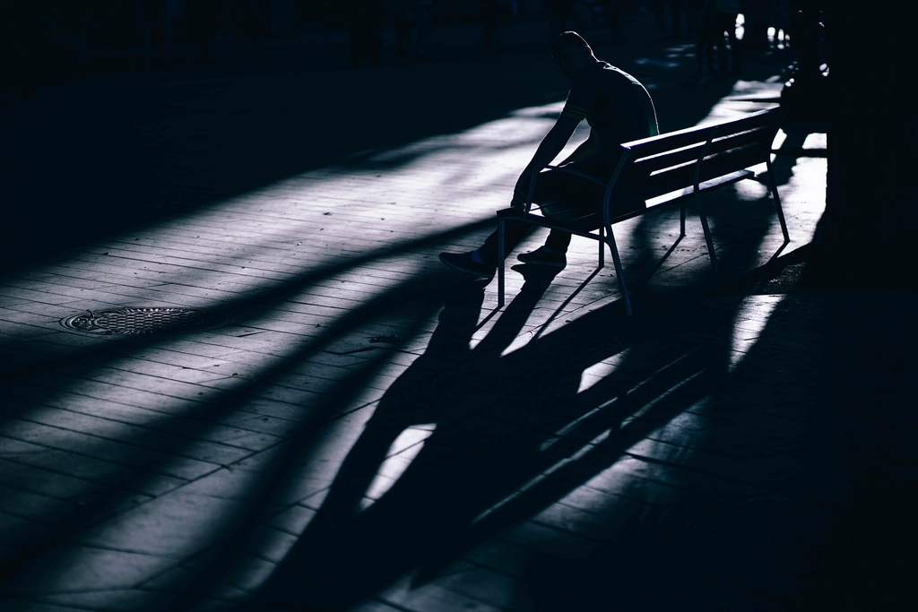 Personne assise seule sur un banc de bois, dos droit, mains posées sur les cuisses