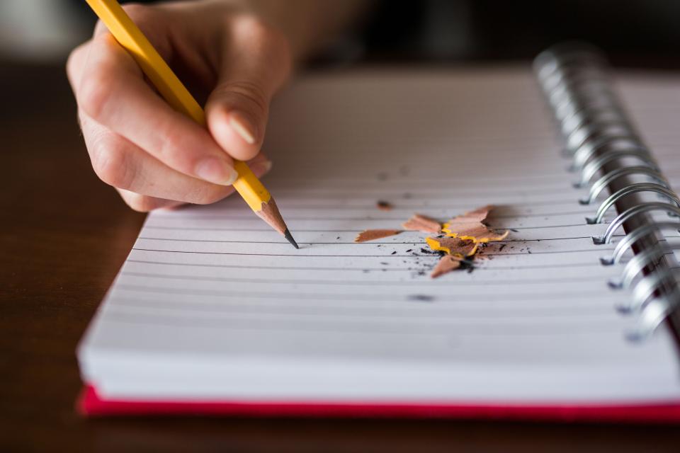 Carnet ouvert et crayon posés sur une table, page quadrillée portant quelques lignes