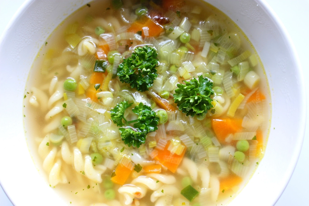 Bol de soupe de légumes fumante posé devant une assiette vide sur une nappe claire
